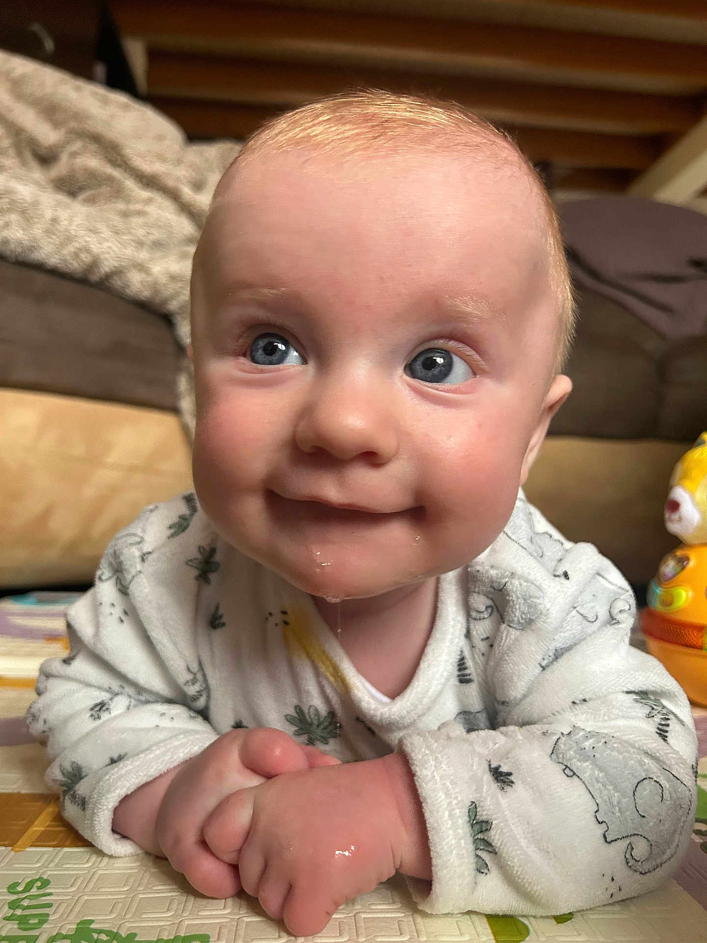 Arthur a rejoint le concours — aidez-le/la à gagner de superbes lots ! baby, infant, child, blue_eyes, drool, onesie, patterned_clothing, close_up, portrait, playmat, clasped_hands, smile, toy, couch, blanket, indoor, floor_mat, cheeks, expression, hand