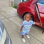 Quadir is registered to the contest to win money with this photo: toddler, child, car, red_car, driveway, clothing, shorts, polo_shirt, white_shoes, bracelet, necklace, sidewalk, outdoor, hairstyle, curious, standing, person, daylight, residential, home