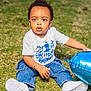 toddler, child, grass, balloon, blue_balloon, white_shoes, jeans, bracelet, necklace, birthday_shirt, outdoor, daylight, cute, sitting, young_child, portrait, celebration, casual_clothing, curious, innocent