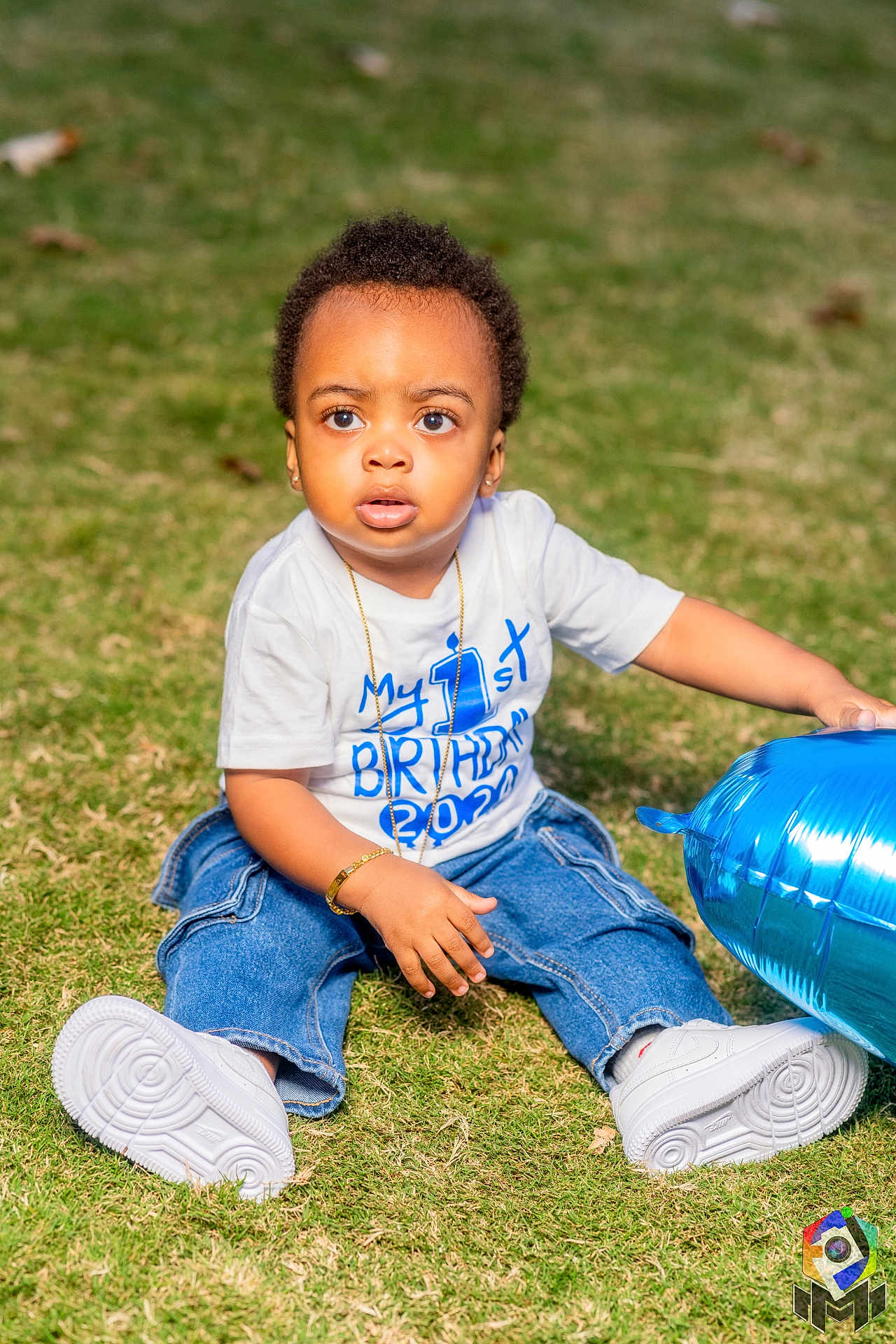 Quadir is registered to the contest to win money with this photo: toddler, child, grass, balloon, blue_balloon, white_shoes, jeans, bracelet, necklace, birthday_shirt, outdoor, daylight, cute, sitting, young_child, portrait, celebration, casual_clothing, curious, innocent