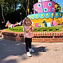 child, toddler, smiling, outdoor, daylight, colorful, decoration, cake, toy, grass, trees, brick_wall, pavement, bunting, shoes, clothing, happy, person, nature, sunlight