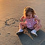 toddler, child, beach, sand, sunset, shadow, ocean, water, waves, dress, white_shoes, footwear, sitting, heart_drawing, sunlight, outdoor, nature, curly_hair, play, person
