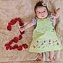 baby, infant, child, flower_clip, green_dress, embroidered_flowers, rose_petals, heart_shape, blanket, soft_texture, cute, lying_down, hands_up, barefoot, indoor, portrait, curious_expression, adorable, skin, head