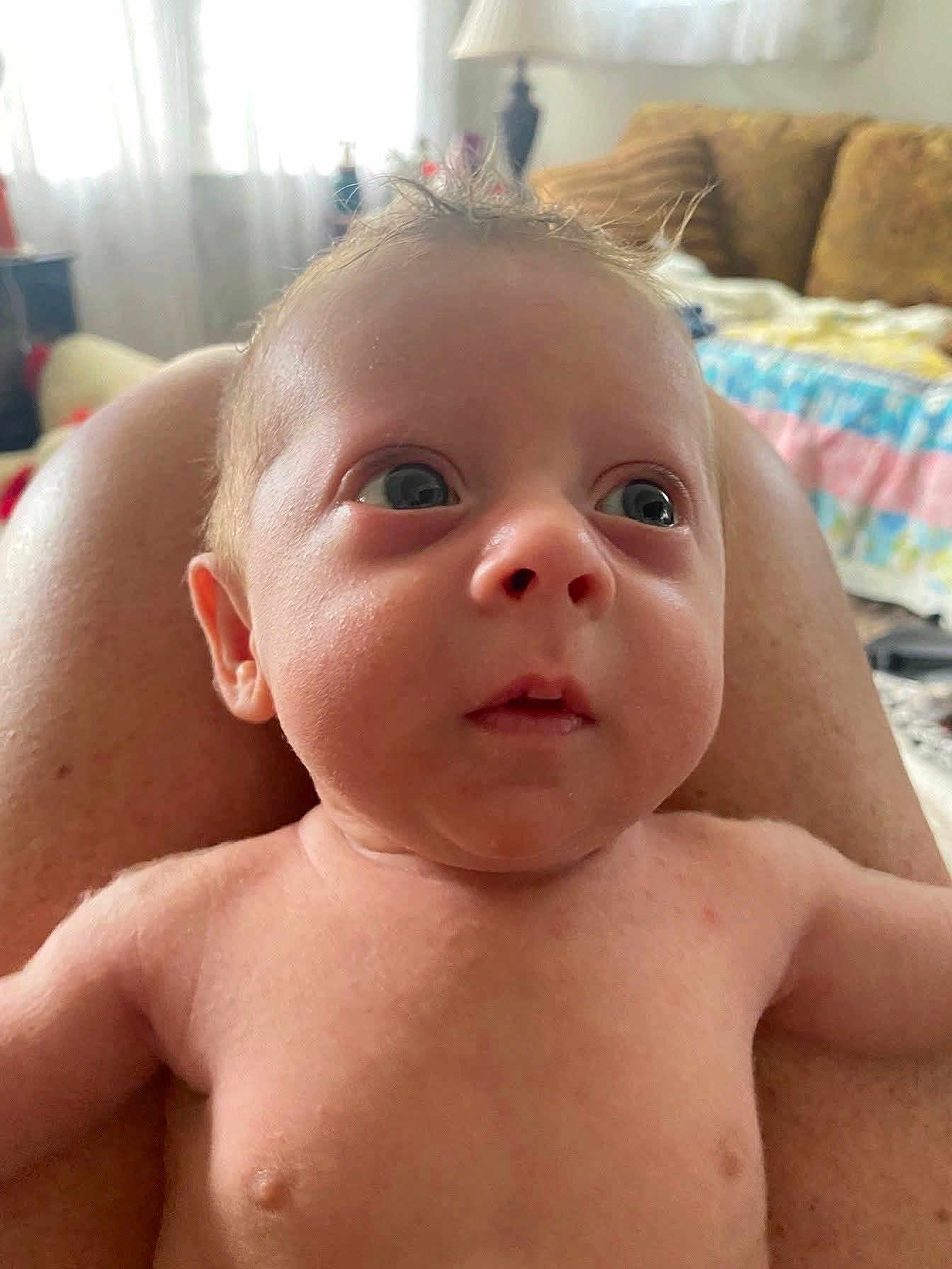 Asher is registered to the contest to win money with this photo: baby, infant, face, skin, person, legs, indoor, living_room, couch, blanket, curly_hair, wide_eyes, expression, close_up, child, human, torso, naked, background, soft_light