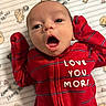 Antonio is registered to the contest to win money with this photo: baby, infant, red_clothing, striped_onesie, face, eyes, mouth_open, blanket, pattern, bear_illustrations, text_on_clothing, lying_down, newborn, cute, expression, small_hands, sleepwear, child, portrait, indoors