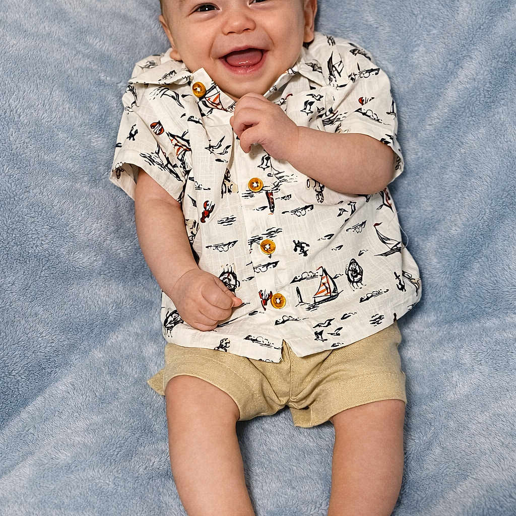 Antonio is registered to the contest to win money with this photo: baby, smiling, infant, child, clothing, shirt, sandals, blanket, happy, cute, portrait, human, footwear, lying_down, young, skin, face, head, one_person, indoors