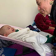 David Mihail joined the competition — help win amazing prizes! baby, blanket, baby_rocker, woman, smile, indoor, bed, purple_bedspread, person, earring, clothing, face, interaction, family, comfort, toddler, infant, adult, blanket_wrap, candid