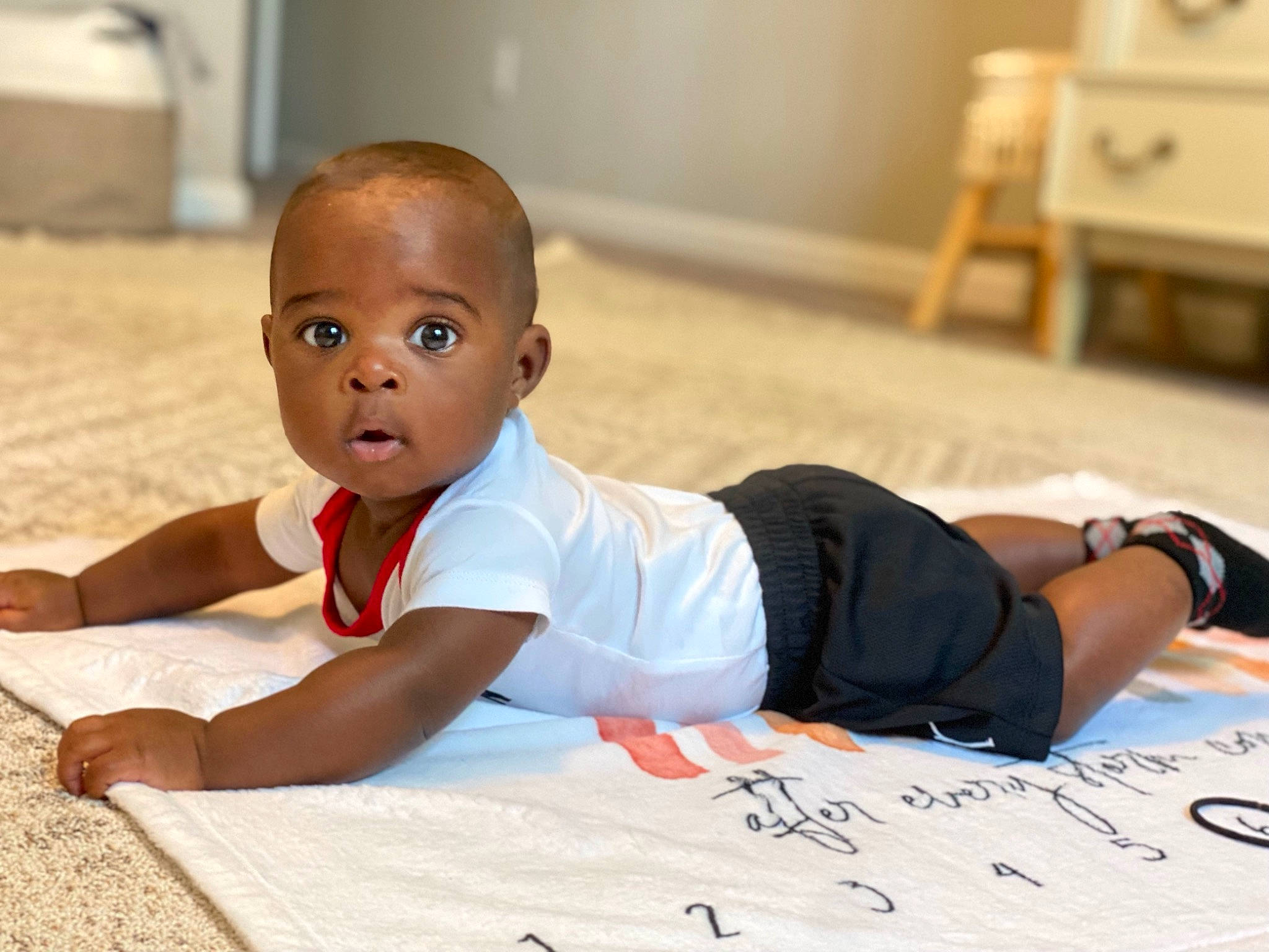 Konnor is registered to the contest to win money with this photo: baby, baby_toddler_clothing, balance, chest, elbow, face, flooring, fun, handwriting, happy, hardwood, human_leg, knee, leisure, person, sitting, sleeve, sportswear, t_shirt, thigh
