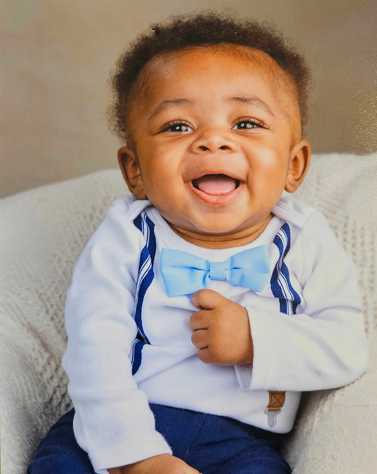 Ahmari joined the competition — help win amazing prizes! baby, smiling, blue_bow_tie, white_shirt, suspenders, infant, happy, portrait, cute, child, indoor, knitted_blanket, seated, young_child, face, person, cheerful, toddler, fashion, closeup
