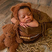 Ahmari is registered to the contest to win money with this photo: baby, bear_hat, brown_cloth, brown_hat, child, cozy, cute, indoors, infant, newborn, peaceful, plush_toy, portrait, resting, rustic_floor, sleeping, soft_texture, teddy_bear, wooden_bucket, woven_rug