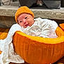 Juliet is registered to the contest to win money with this photo: baby, pumpkin, orange_hat, blanket, white_clothing, infant, cozy, fall, autumn, carved_pumpkin, wood_floor, rug, indoor, cute, smiling, face, small_pumpkin, knit_hat, child, person