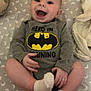 Dominick is registered to the contest to win money with this photo: baby, infant, smiling, batman_logo, onesie, socks, diaper, happy, lying_down, bed, pillow, moon_pattern, child, cute, playful, clothing, human, portrait, indoor, expression
