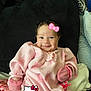 baby, infant, pink_clothing, mittens, smile, cute, cozy, blanket, cushion, indoors, lying_down, face, head, child, soft_texture, hello_kitty, graphic_overlay, happy, portrait, warm