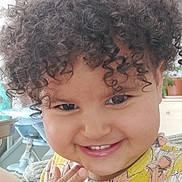 Léa a rejoint le concours — aidez-le/la à gagner de superbes lots ! child, smile, curly_hair, hand, face, indoor, happy, person, cute, toddler, clothing, patterned_shirt, portrait, skin, furniture, plant, background, light, closeup, expression