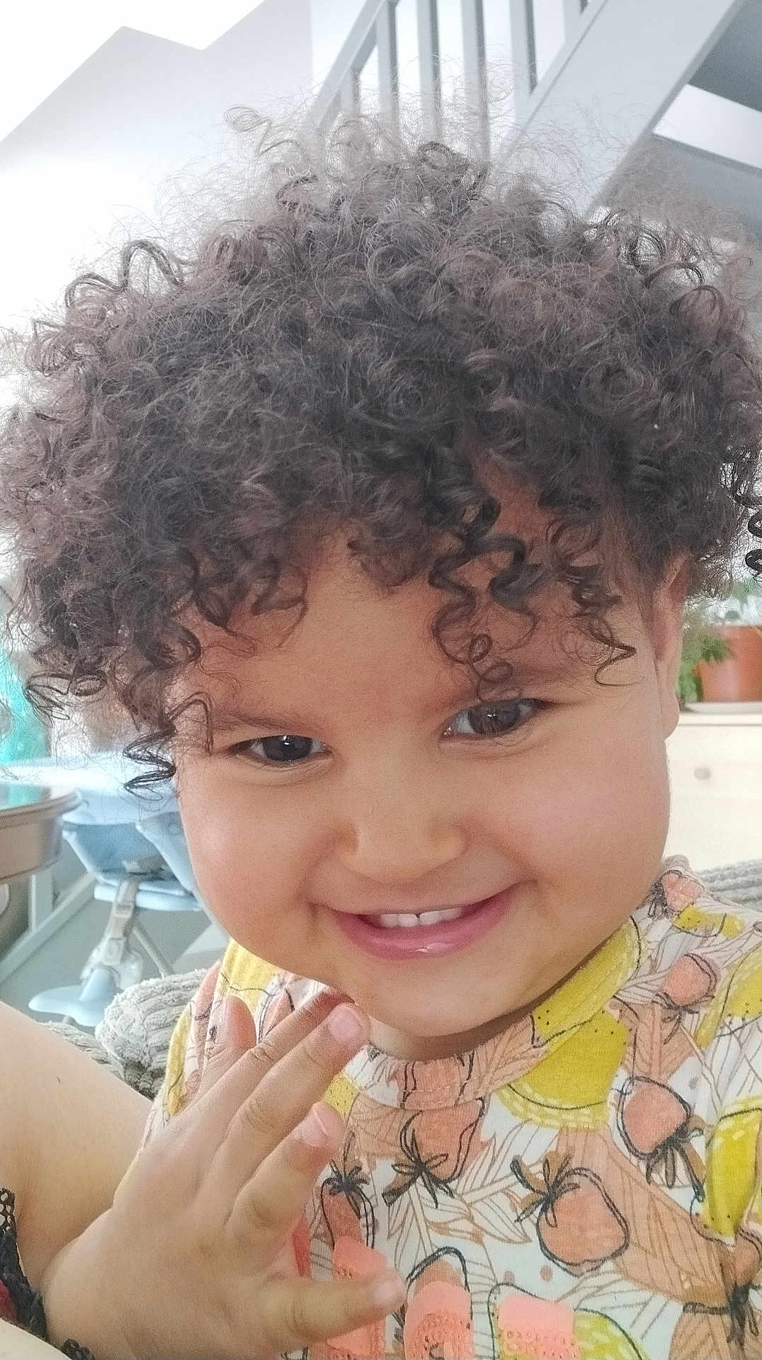 Léa a rejoint le concours — aidez-le/la à gagner de superbes lots ! child, smile, curly_hair, hand, face, indoor, happy, person, cute, toddler, clothing, patterned_shirt, portrait, skin, furniture, plant, background, light, closeup, expression