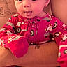 baby, child, infant, portrait, face, smiling, tongue, wide_eyed, pink_clothing, pajamas, onesie, vehicle_pattern, adult, hands, holding, indoor, closeup, sitting, cozy, photography