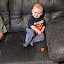 toddler, child, smiling, black_couch, pacifier, clothing, socks, pants, tshirt, indoor, furniture, person, cute, playful, seated, home, living_room, young_child, happy, casual