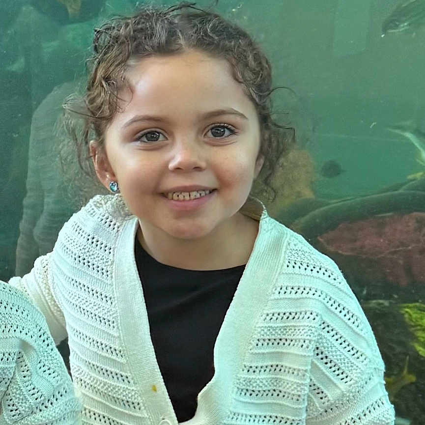 Kenli is registered to the contest to win money with this photo: aquarium, black_shirt, child, clothing, curly_hair, cute, earrings, eyebrows, eyes, face, fish, girl, happy, indoors, person, portrait, smiling, water, white_cardigan, young