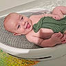 baby, bath, water, green_cloth, smiling, tongue_out, bath_basket, infant, skin, playful, child, splashing, happy, toddler, bathtub, cute, young, person, relaxing, home