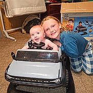 Michael is registered to the contest to win money with this photo: baby, box, car, car_seat, carpet, child, clothing, face, floor, furniture, hair, happy, indoor, person, play, room, sibling, smile, toy_car, vehicle