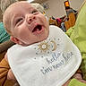 Michael is registered to the contest to win money with this photo: baby, infant, bib, smiling, person, indoor, holding, clothing, face, head, people, furniture, wood, light, happy, child, newborn, casual, seated, warm_lighting