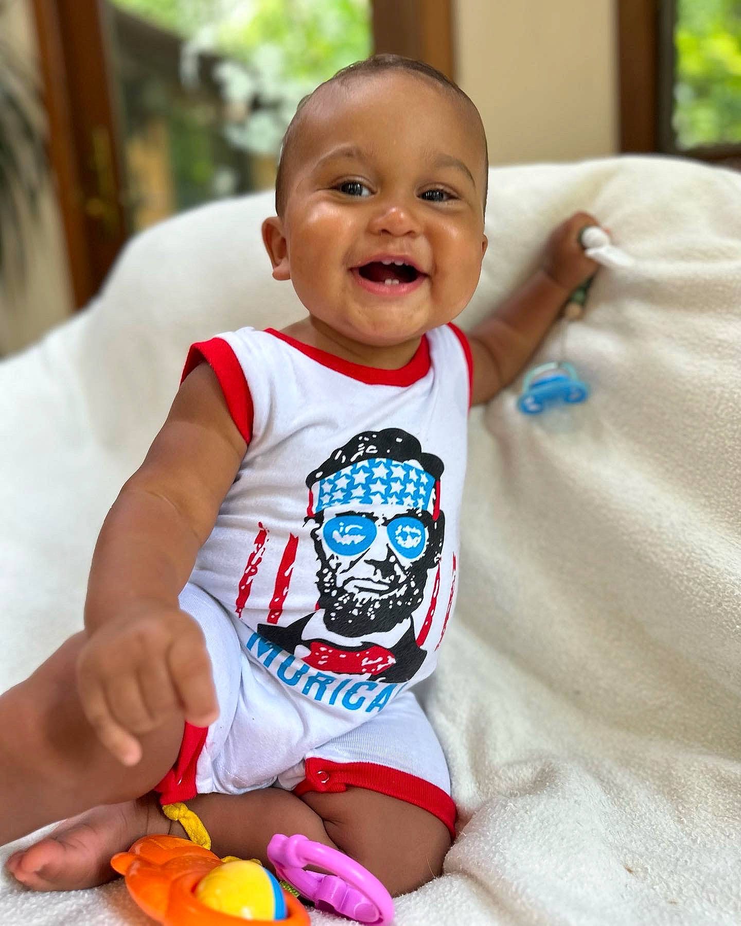 Cairo is registered to the contest to win money with this photo: arm, baby, baby_toddler_clothing, cheek, child, comfort, face, finger, fun, hand, happy, head, person, sitting, skin, sleeve, smile, t_shirt, textile, thigh