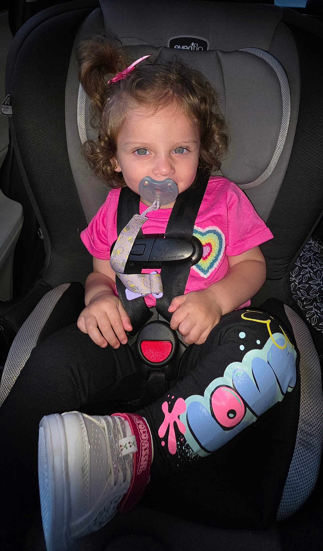 Eimy is registered to the contest to win money with this photo: toddler, child, car_seat, pacifier, pink_shirt, heart_design, leggings, sneakers, curly_hair, hair_clip, safety_harness, car_interior, seatbelt, cute, young_child, portrait, indoor, casual_clothing, footwear, baby