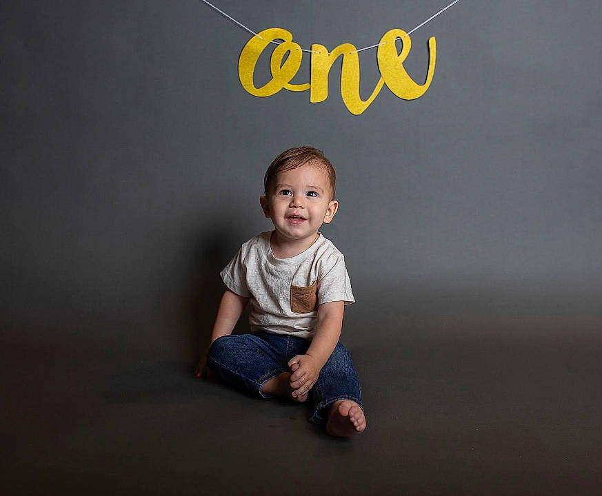 Kash is registered to the contest to win money with this photo: art, baby, baby_toddler_clothing, brand, child, electric_blue, flash_photography, flooring, font, graphics, happy, joy, logo, pattern, person, portrait_photography, sitting, sleeve, smile, t_shirt