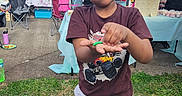 Jeremy is registered to the contest to win money with this photo: banner, boy, celebration, chair, child, clothing, curious, daylight, event, face, footwear, grass, hand, outdoor, party, people, shorts, table, tshirt, umbrella