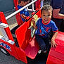 adult, blue_shirt, boy, casual_clothing, child, concrete, daytime, fire_truck, fun, happy, outdoor, person, play, playground, red, seat, smile, sunlight, toy, wood