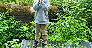 Jeremy is registered to the contest to win money with this photo: casual_clothing, child, curly_hair, daylight, explorer, foliage, forest, greenery, hoodie, metal_platform, nature, outdoor, pants, peaceful, plants, portrait, shoes, standing, wildflowers, young_boy