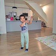 Jeremy is registered to the contest to win money with this photo: child, umbrella, indoor, kitchen, play_mat, wood_floor, socks, casual_clothing, smiling, standing, modern_interior, appliances, cabinet, refrigerator, microwave, lighting, door, shoes, plant, person