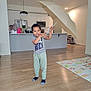 child, umbrella, indoor, kitchen, play_mat, wood_floor, socks, casual_clothing, smiling, standing, modern_interior, appliances, cabinet, refrigerator, microwave, lighting, door, shoes, plant, person