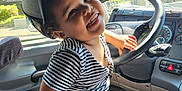 Jeremy joined the competition — help win amazing prizes! toddler, child, smiling, striped_shirt, cap, vehicle_interior, steering_wheel, sunlight, window, seat, dashboard, happy, playful, casual_clothing, hand, face, headwear, seatbelt, person, indoors