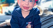 Oakley is registered to the contest to win money with this photo: baby, bed, blue_eyes, child, clothing, cozy, cute, face, happy, headwear, hoodie, indoor, infant, person, pink_socks, portrait, red_bow, sitting, smiling, young_child