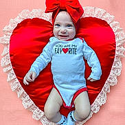 Oakley is registered to the contest to win money with this photo: baby, blue_eyes, child, cute, happy, headband, heart_pillow, indoor, infant, lace, lying_down, onesie, pink_background, portrait, red_bow, red_trim, smiling, socks, soft_texture, white_clothing