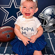 Oakley joined the competition — help win amazing prizes! baby, blue_skirt, bow, carpet, celebration, child, clothing, cowboys, cute, football, happy, headband, helmet, indoor, person, portrait, smiling, sports, team_spirit, toddler