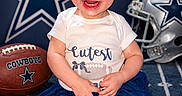 Oakley joined the competition — help win amazing prizes! baby, blue_skirt, bow, carpet, celebration, child, clothing, cowboys, cute, football, happy, headband, helmet, indoor, person, portrait, smiling, sports, team_spirit, toddler