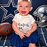 baby, blue_skirt, bow, carpet, celebration, child, clothing, cowboys, cute, football, happy, headband, helmet, indoor, person, portrait, smiling, sports, team_spirit, toddler