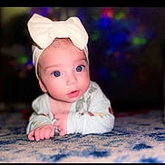 Oakley joined the competition — help win amazing prizes! baby, blue_eyes, bow, carpet, child, closeup, colorful_bokeh, curious_expression, cute, face, headband, indoor, infant, long_sleeve_clothing, lying_down, patterned_rug, portrait, skin, soft_lighting, young_child