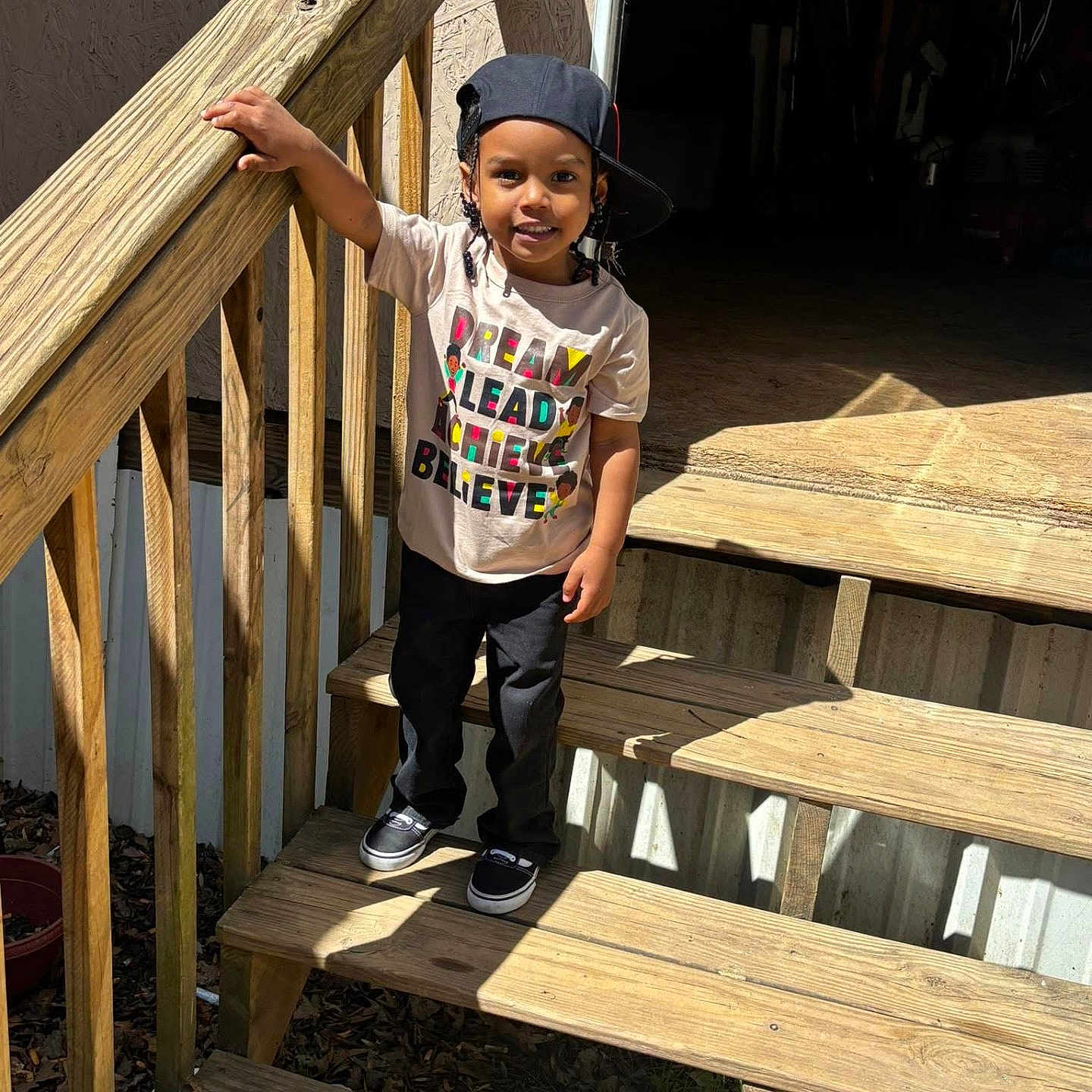 Amari is registered to the contest to win money with this photo: boy, cap, casual_clothing, child, daylight, feet, handrail, happy, outdoor, person, portrait, shadow, shoes, smile, stairs, standing, sunlight, tshirt, wooden_stairs, young