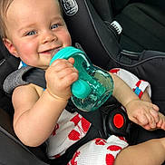 Judah is registered to the contest to win money with this photo: baby, child, car_seat, blue_eyes, smiling, sippy_cup, teal, white_outfit, red_pattern, seatbelt, infant, cute, happy, holding, hand, car_interior, portrait, closeup, comfort, safety