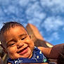 baby, smiling, child, blue_sky, clouds, outdoor, portrait, happy, face, skin, sleeveless, person, closeup, sunlight, cheeks, arm, holding, infant, cute, daytime