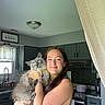 Cornelius Aka Corn is registered to the contest to win money with this photo: woman, cat, indoor, kitchen, smiling, holding, pet, gray_cat, blue_eyes, long_hair, casual_clothing, window, curtains, cabinet, countertop, stove, light_fixture, watch, bracelet, appliance