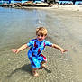 child, boy, water, beach, swimsuit, spiderman, splashing, sand, sunny, daylight, shore, palm_tree, bridge, rocks, cars, outdoor, playing, happy, vacation, summer