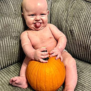 Matthew is registered to the contest to win money with this photo: baby, pumpkin, tongue_out, couch, gray_couch, bare_chest, infant, sitting, happy, playful, indoors, cute, chubby, skin, hand, foot, smile, expression, holding, furniture