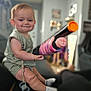 baby, child, toy_gun, indoor, sitting, smiling, cute, socks, pacifier, green_clothing, face, person, home, furniture, blurred_background, living_room, infant, happy, playful, short_hair