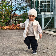 Keylann participe au concours pour gagner de l'argent avec cette photo : toddler, child, boy, walking, hat, vest, sweater, pants, sneakers, outdoor, autumn, leaves, tree, fence, sidewalk, smile, person, daylight, nature, casual_clothing
