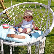 Nilo a rejoint le concours — aidez-le/la à gagner de superbes lots ! baby, child, cushion, daytime, garden, grass, greenery, happy, hat, macrame, nature, outdoor, person, playground, relaxing, seat, smile, summer, sunlight, swing