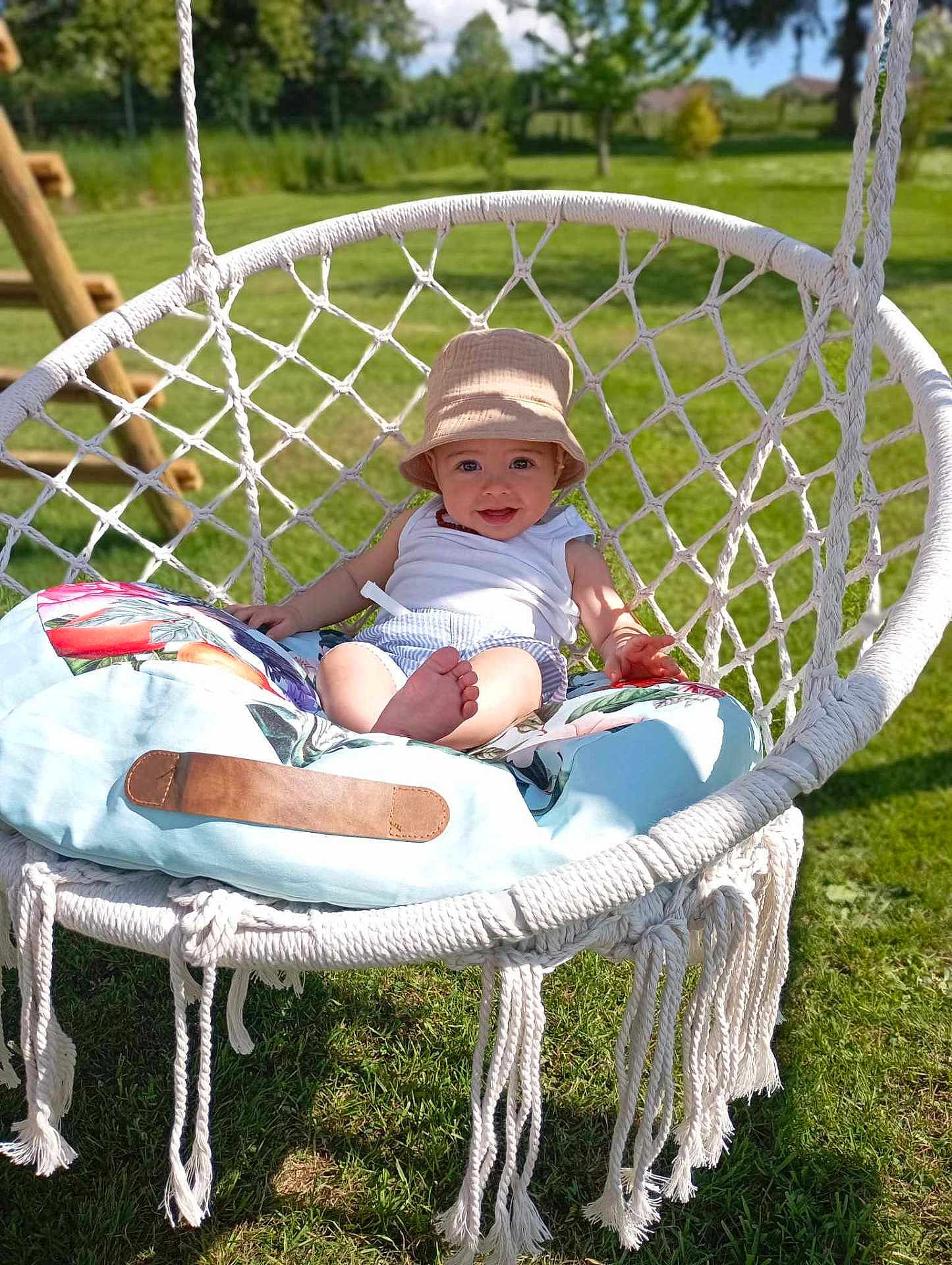 Nilo a rejoint le concours — aidez-le/la à gagner de superbes lots ! baby, child, cushion, daytime, garden, grass, greenery, happy, hat, macrame, nature, outdoor, person, playground, relaxing, seat, smile, summer, sunlight, swing